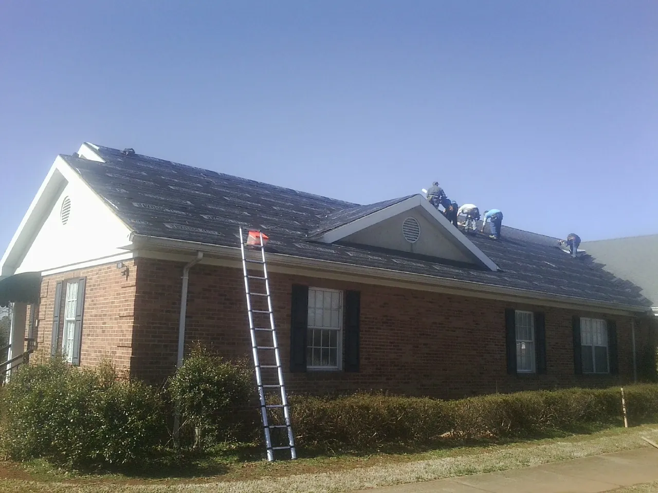 Crew tearing shingles off a brick ranch roof with a ladder set — Emergency Roof Repair work by our crew in Ethridge