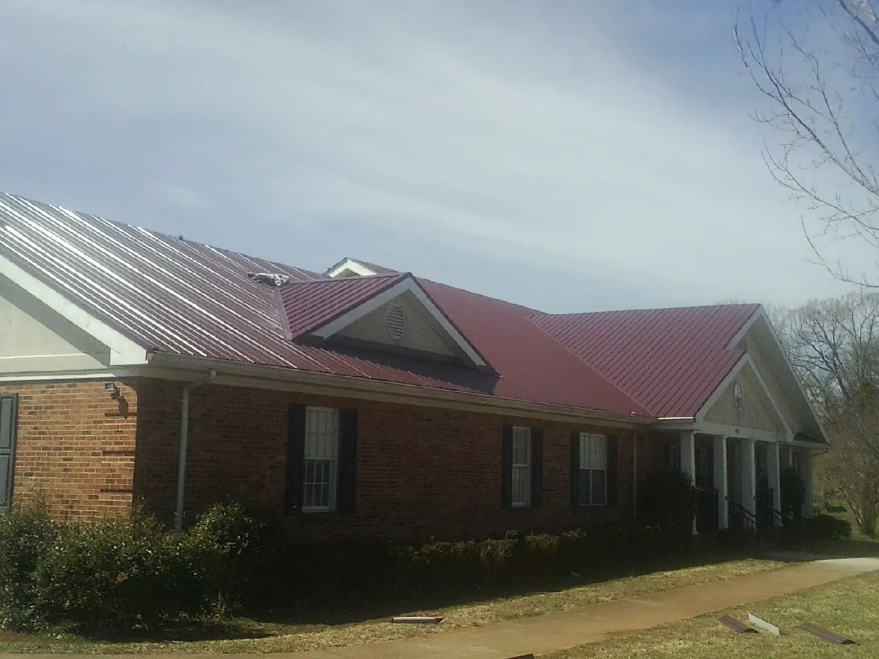 Red metal roof with gabled entries on a long brick building, from a Hail Damage Roof Repair job in Ethridge