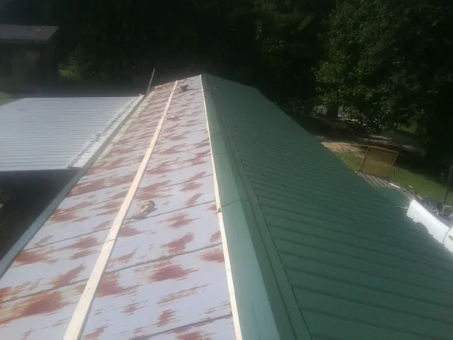 Old rusted panels beside newly installed green metal roofing — Wind Damage Roof Repair by Roofing Brothers in Ethridge