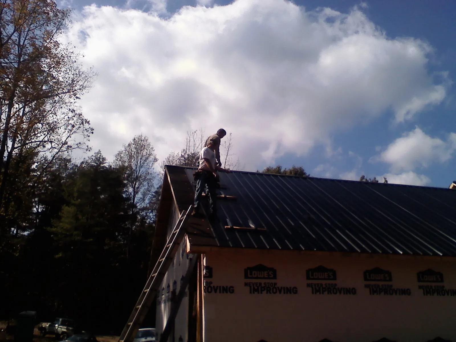 Roofer fastening dark metal panels high against a cloudy sky, from a Roof Inspection job in Ethridge