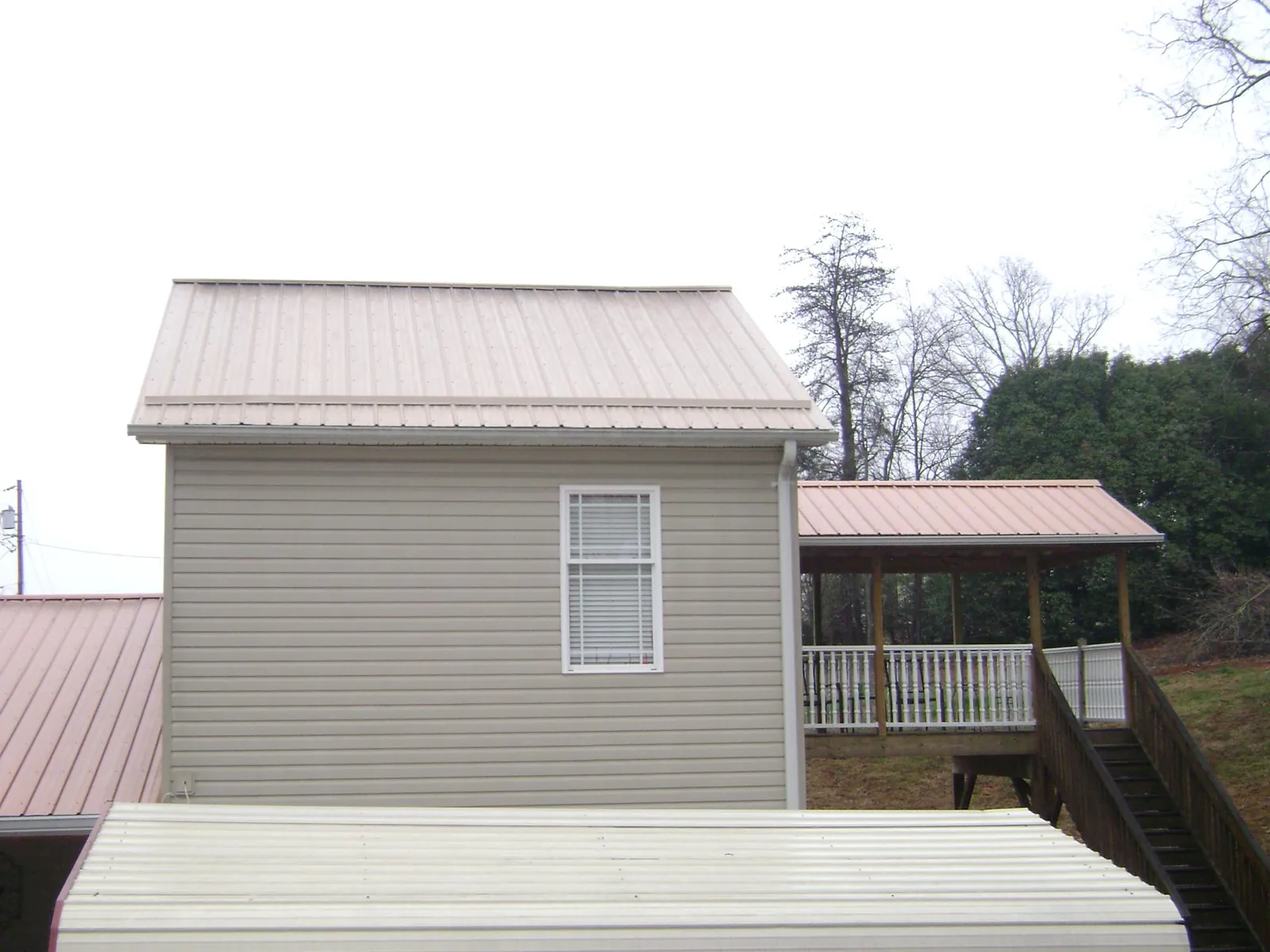 Tan metal roofs on a two story addition and attached porch, from a Roof Replacement job in Ethridge